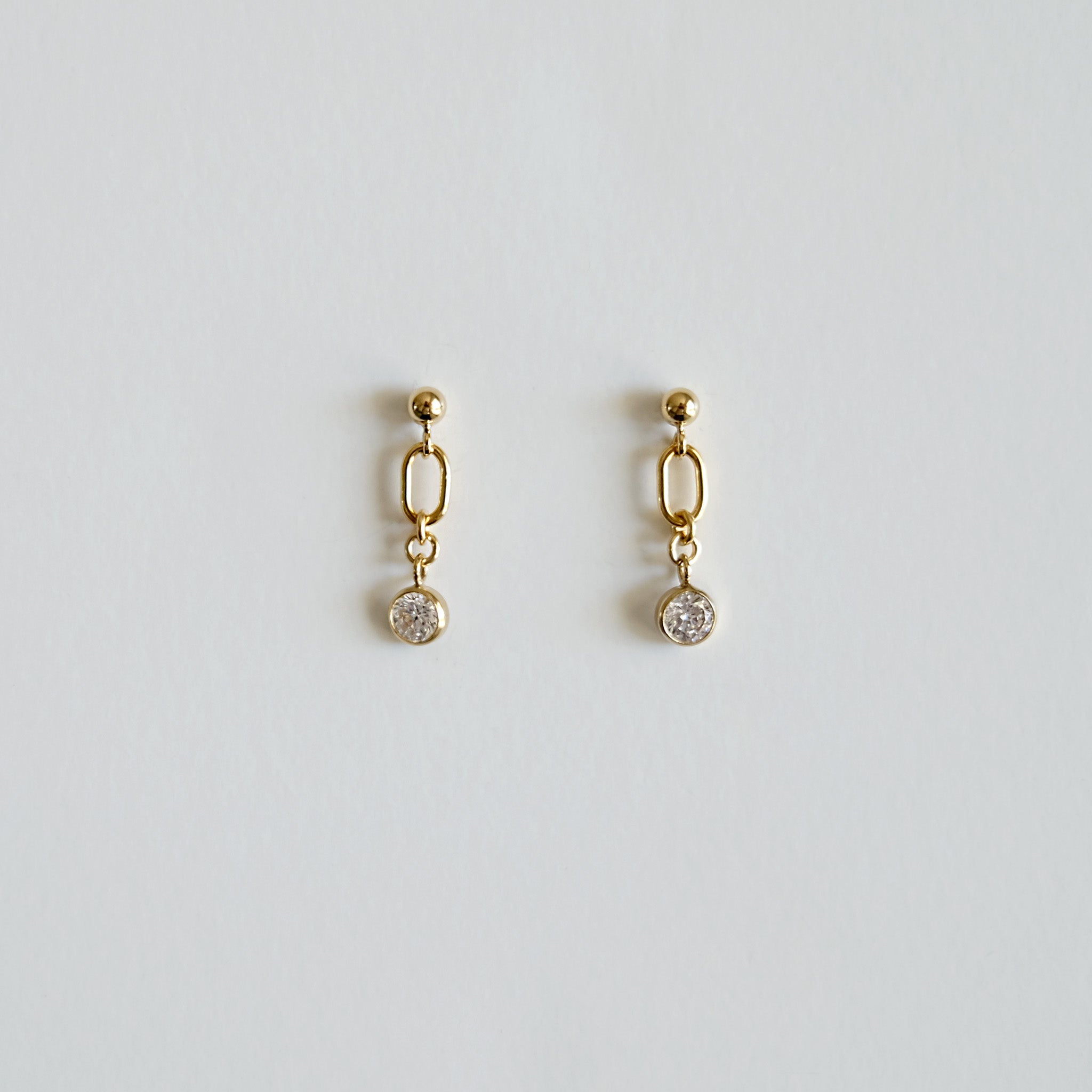 Gold earrings with small round stones on a light gray background