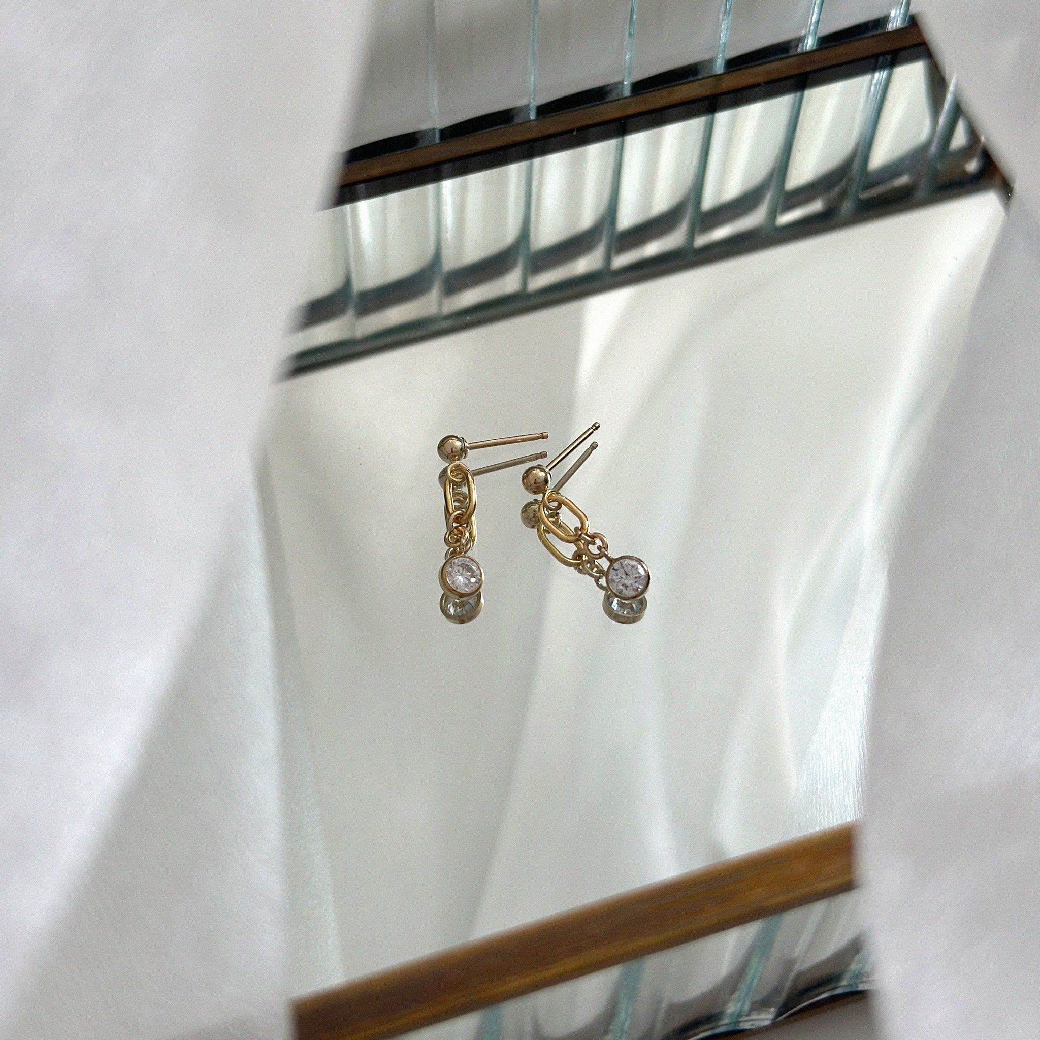 Gold earrings with cubic zirconia pendant on a white background
