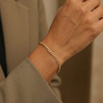 Gold chain bracelet on a wrist with a neutral background
