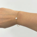 Gold bracelet with a mother of pearl initial charm on a wrist against a white background