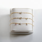 Set of gold filled custom bracelets with small charms on a white bracelet holder
