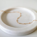 Dotty Chain II Anklet styled on a soft light pink tray, highlighting delicate gold bead accents