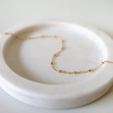Dotty Chain II Anklet styled on a soft light pink tray, highlighting delicate gold bead accents