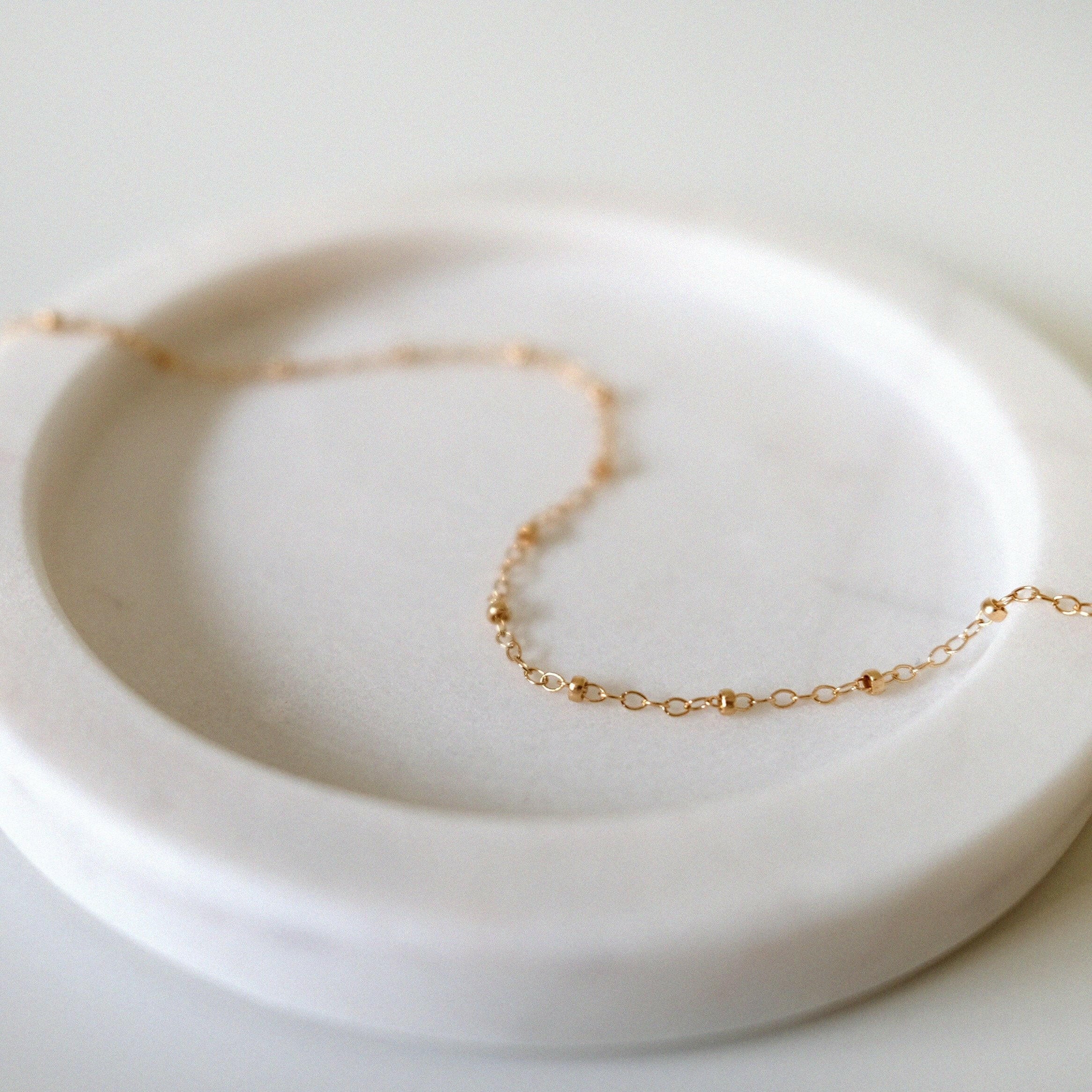 Dotty Chain II Anklet styled on a soft light pink tray, highlighting delicate gold bead accents