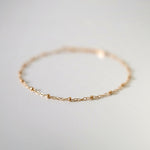 Macro shot focusing on front section of anklet chain with gold beads in sharp detail, background softly blurred