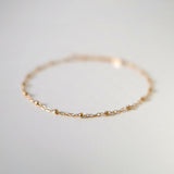 Macro shot focusing on front section of anklet chain with gold beads in sharp detail, background softly blurred