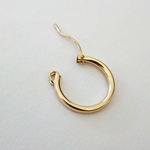 Gold-filled hoop earring laid flat on a white surface, showcasing its polished shine and curved structure