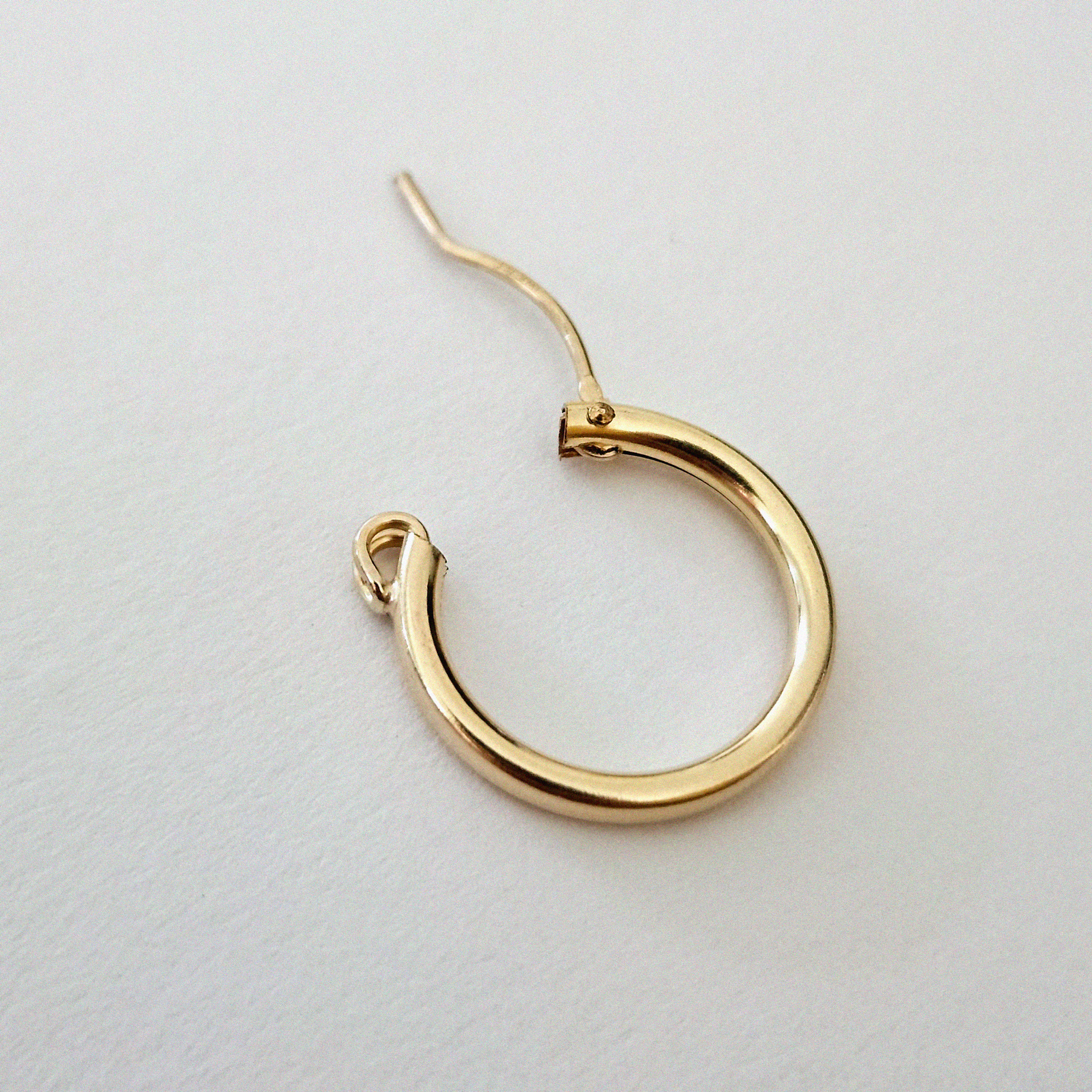 Gold-filled hoop earring laid flat on a white surface, showcasing its polished shine and curved structure