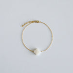 Gold bracelet with a clover-shaped charm on a light gray background