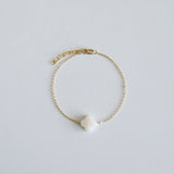 Gold bracelet with a clover-shaped charm on a light gray background