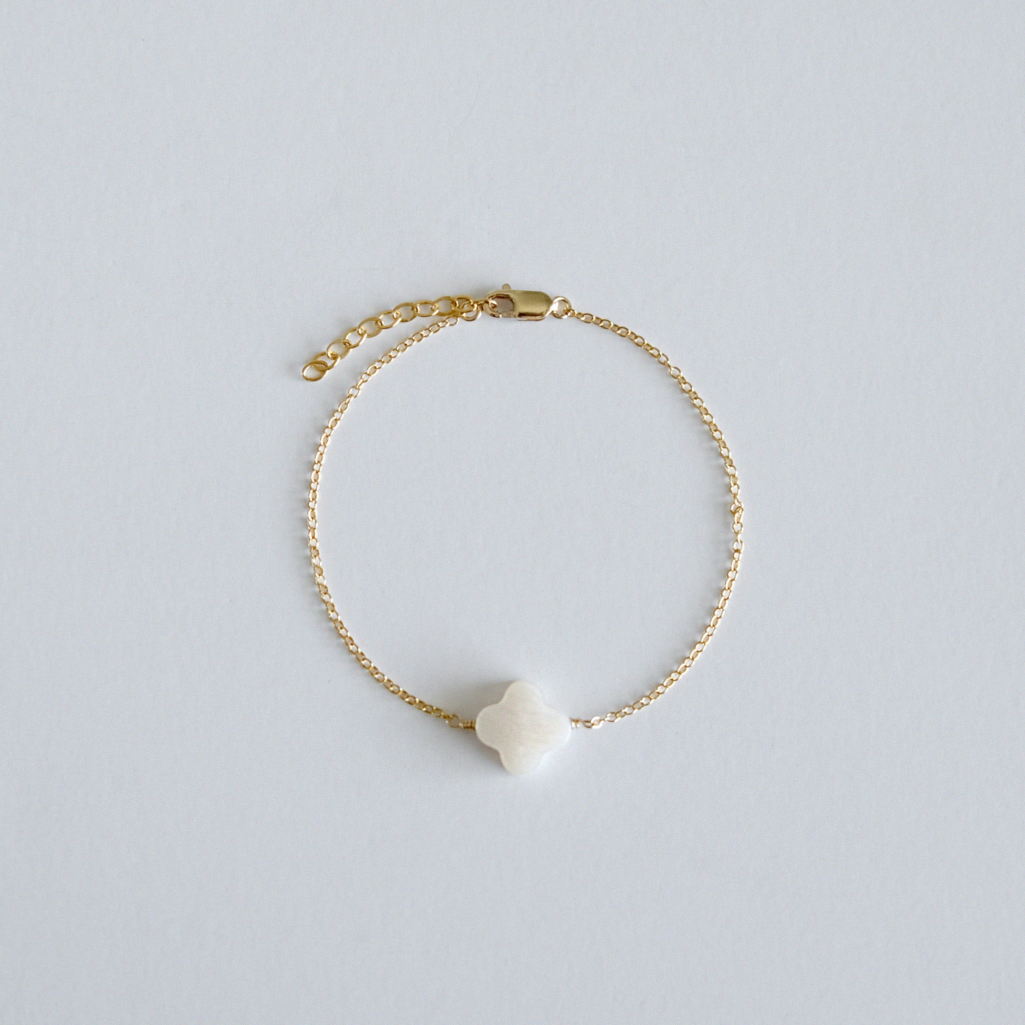 Gold bracelet with a clover-shaped charm on a light gray background