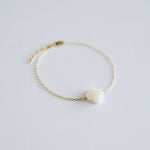 Gold bracelet with a small white stone on a light gray background