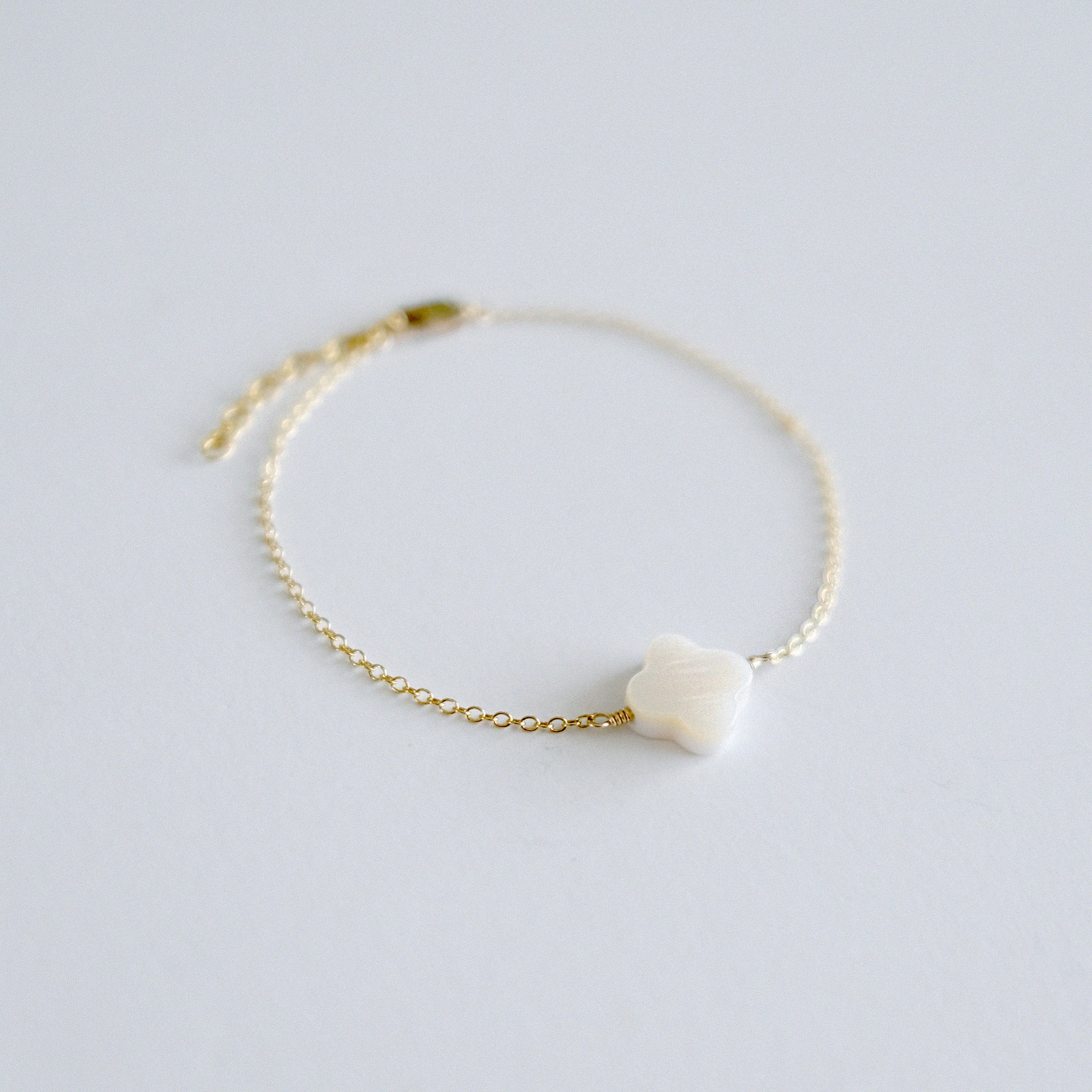 Gold bracelet with a small white stone on a light gray background