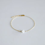 Gold bracelet with a white pearl on a light gray background