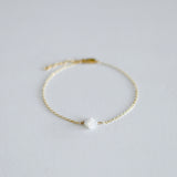 Gold bracelet with a white pearl on a light gray background