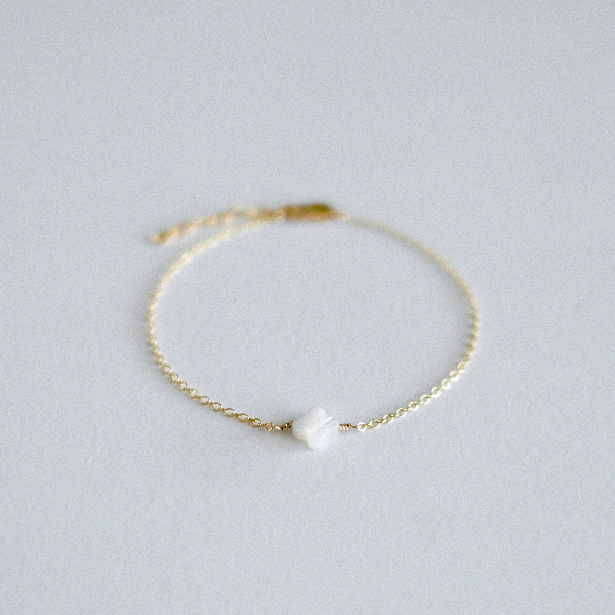 Gold bracelet with a white pearl on a light gray background
