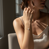 Woman wearing a delicate bracelet with a small clover-shaped charm, sitting in soft light.