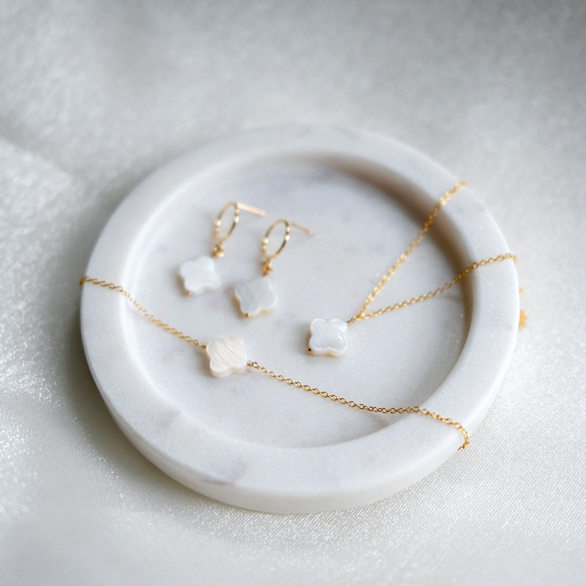 Jewelry set with gold necklaces and earrings on a marble dish.