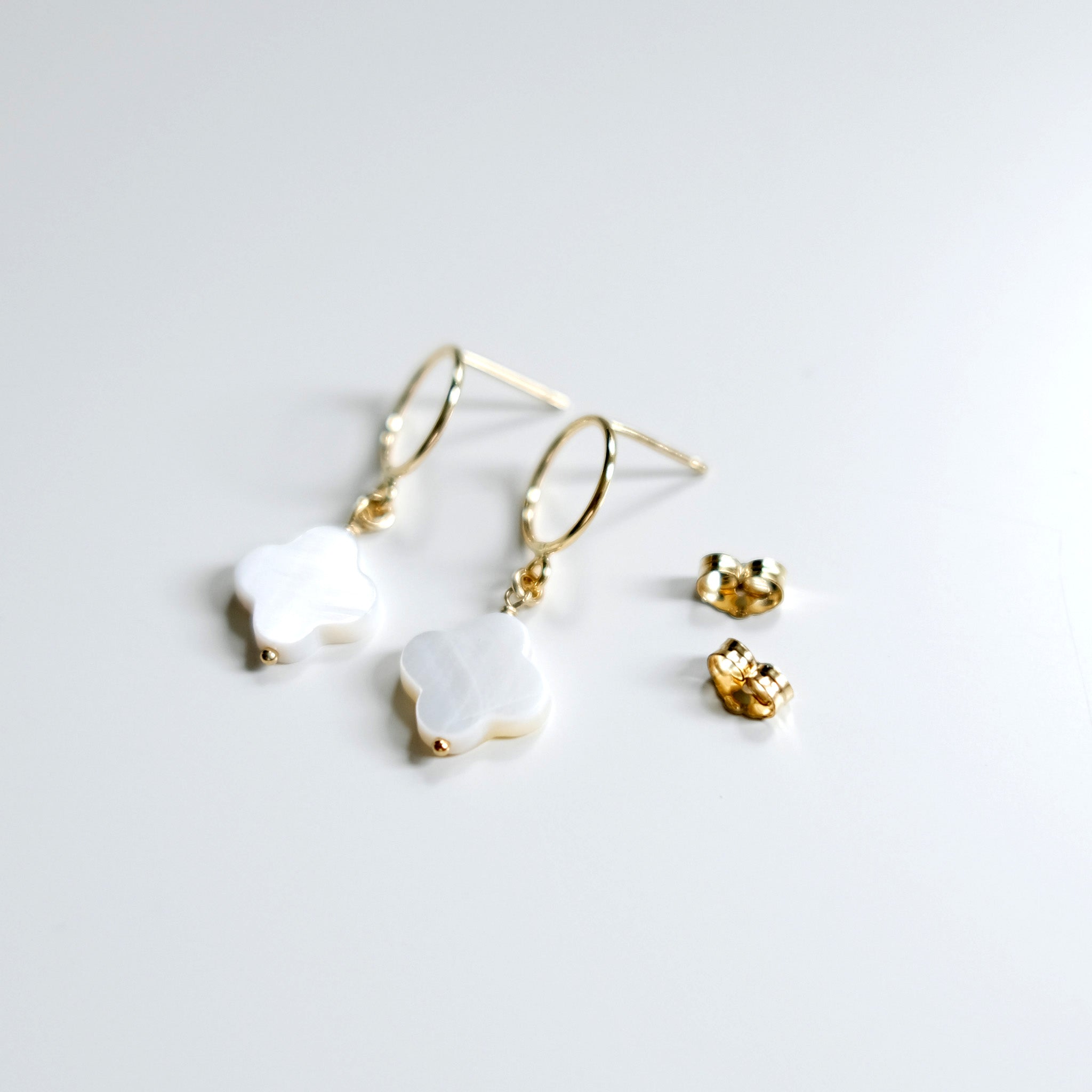 Pair of clover pendant earrings with butterfly back closures on a light gray background