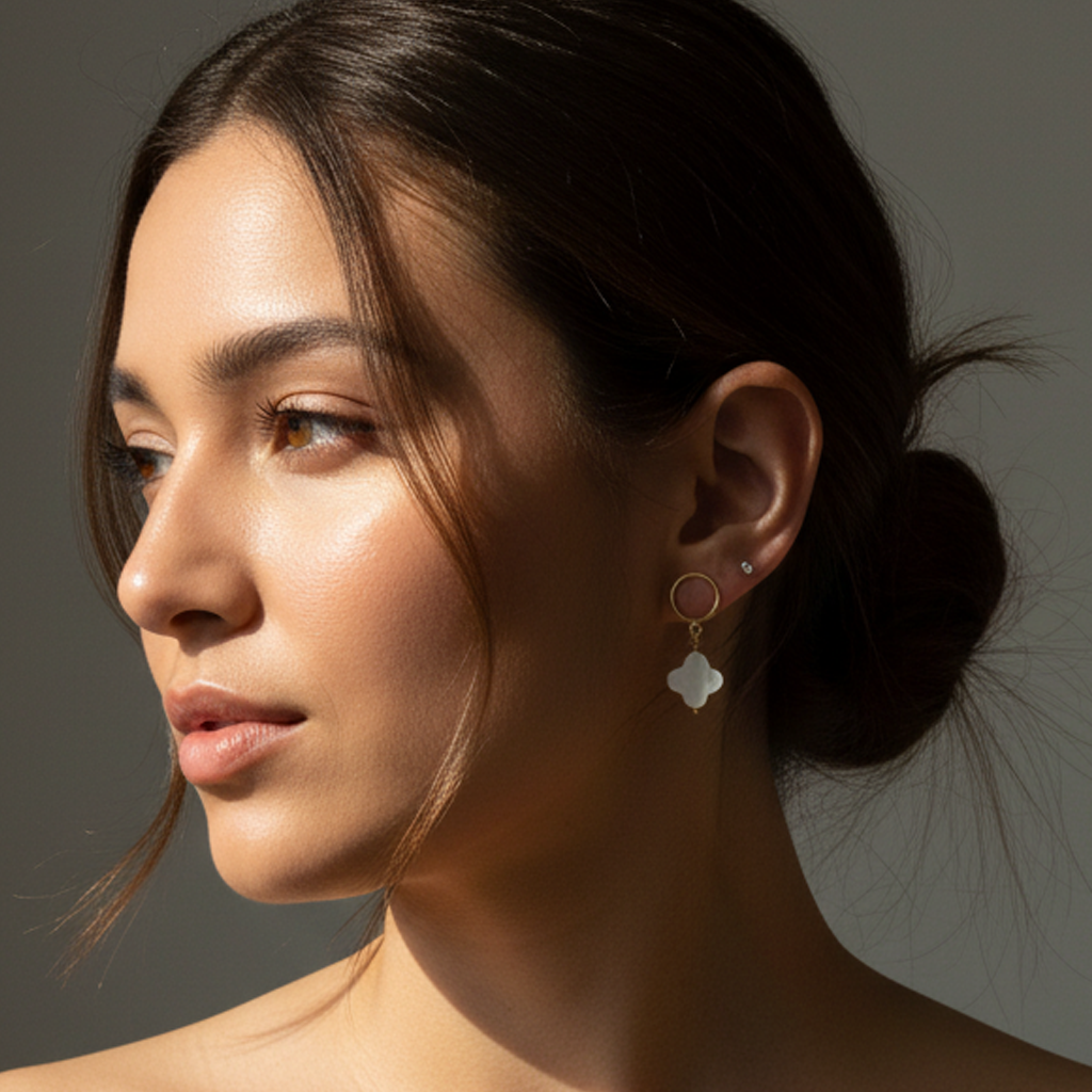 Close-up of a woman wearing mother of pearl clover pendant earrings with a neutral background