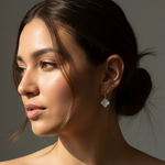 Close-up of a woman wearing mother of pearl clover pendant earrings with a neutral background