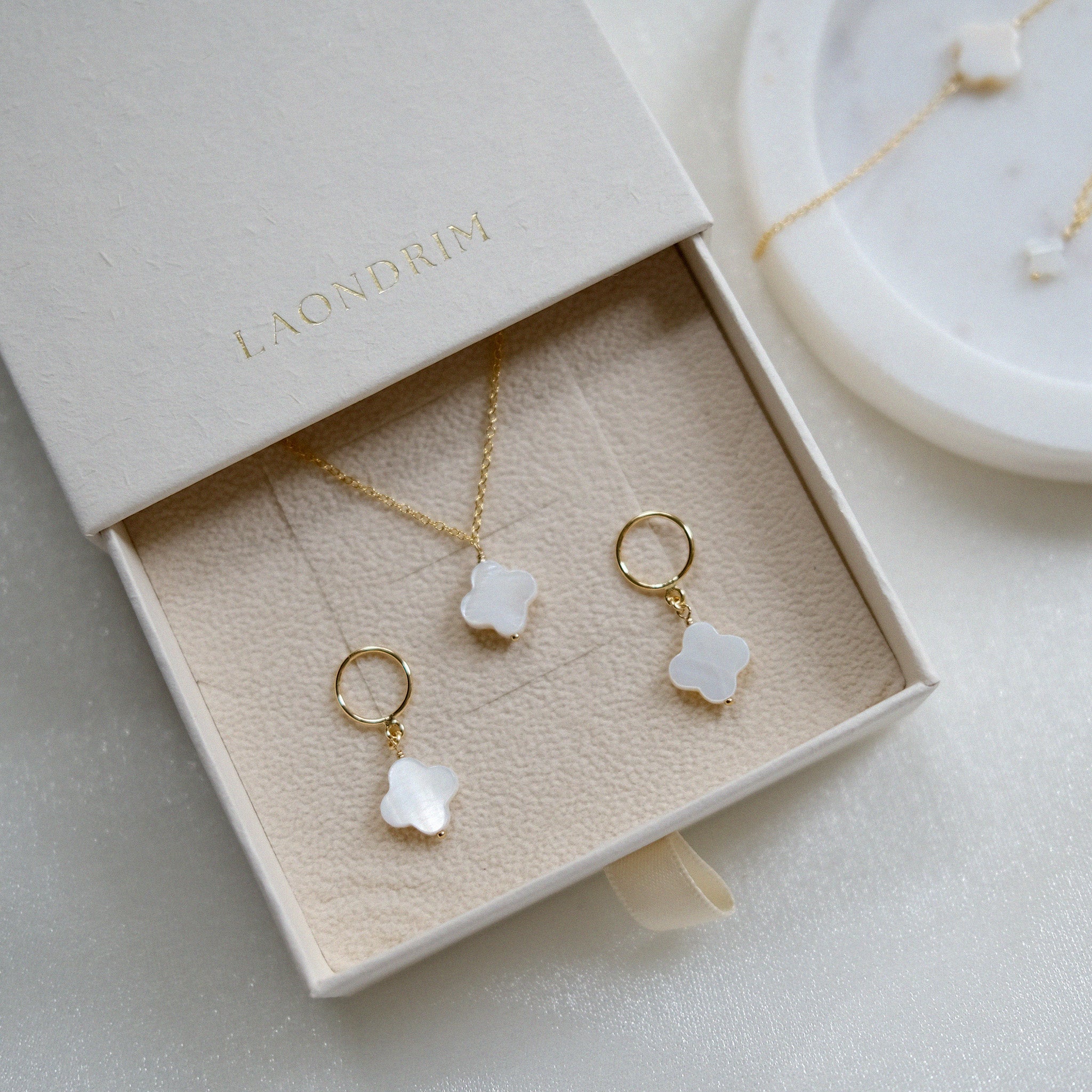 Jewelry set with gold necklaces and earrings in a 'LAONDRIM' box on a light background