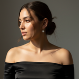 Woman wearing a black off-shoulder top against a gray background and wearing a clover charm earrings