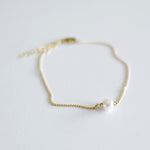 Gold bracelet with a single pearl on a light gray background