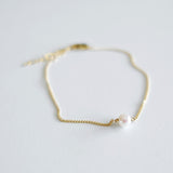 Gold bracelet with a single pearl on a light gray background