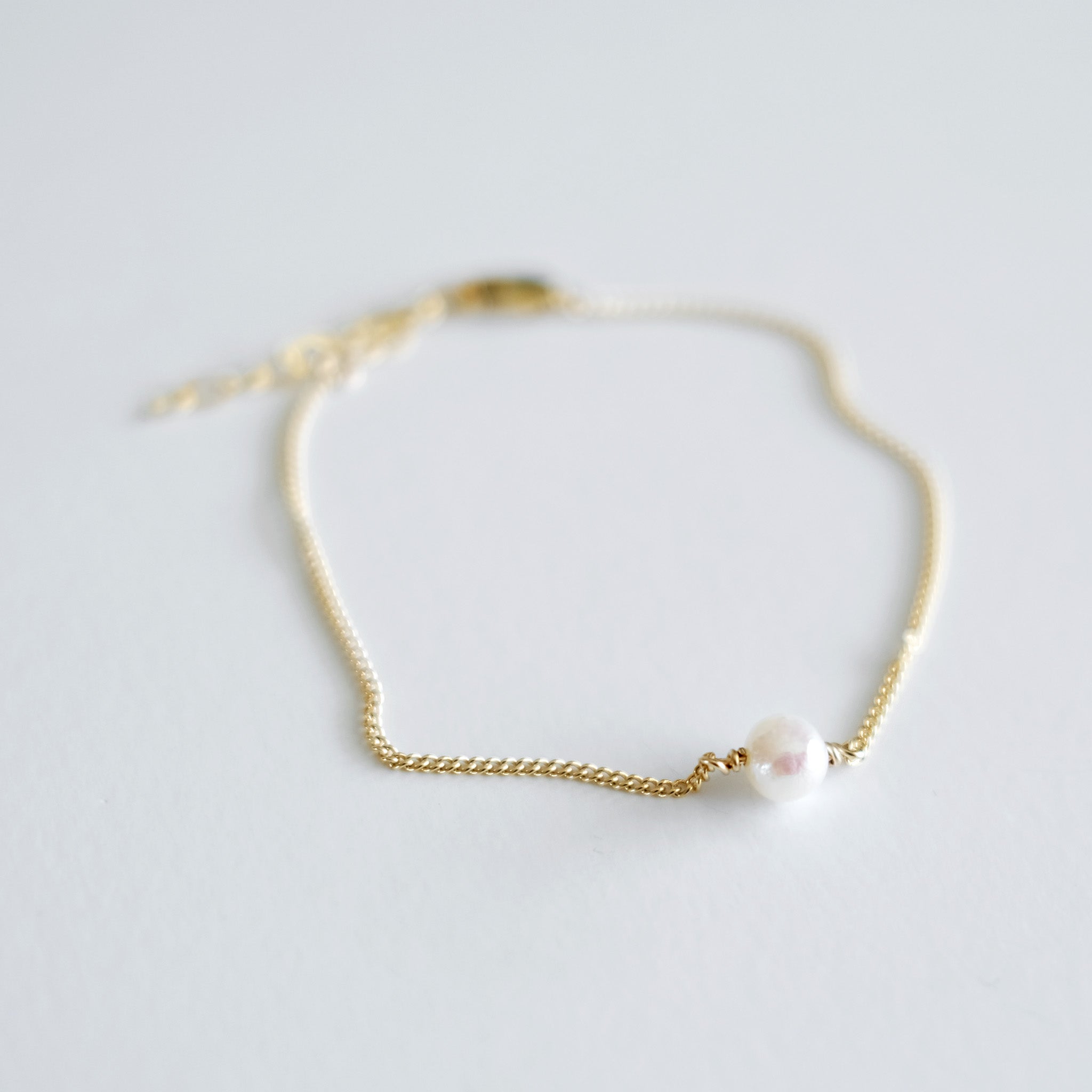 Gold bracelet with a single pearl on a light gray background