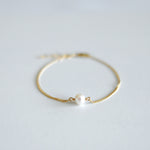 Gold bracelet with a pearl on a light gray background