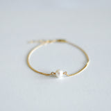 Gold bracelet with a pearl on a light gray background