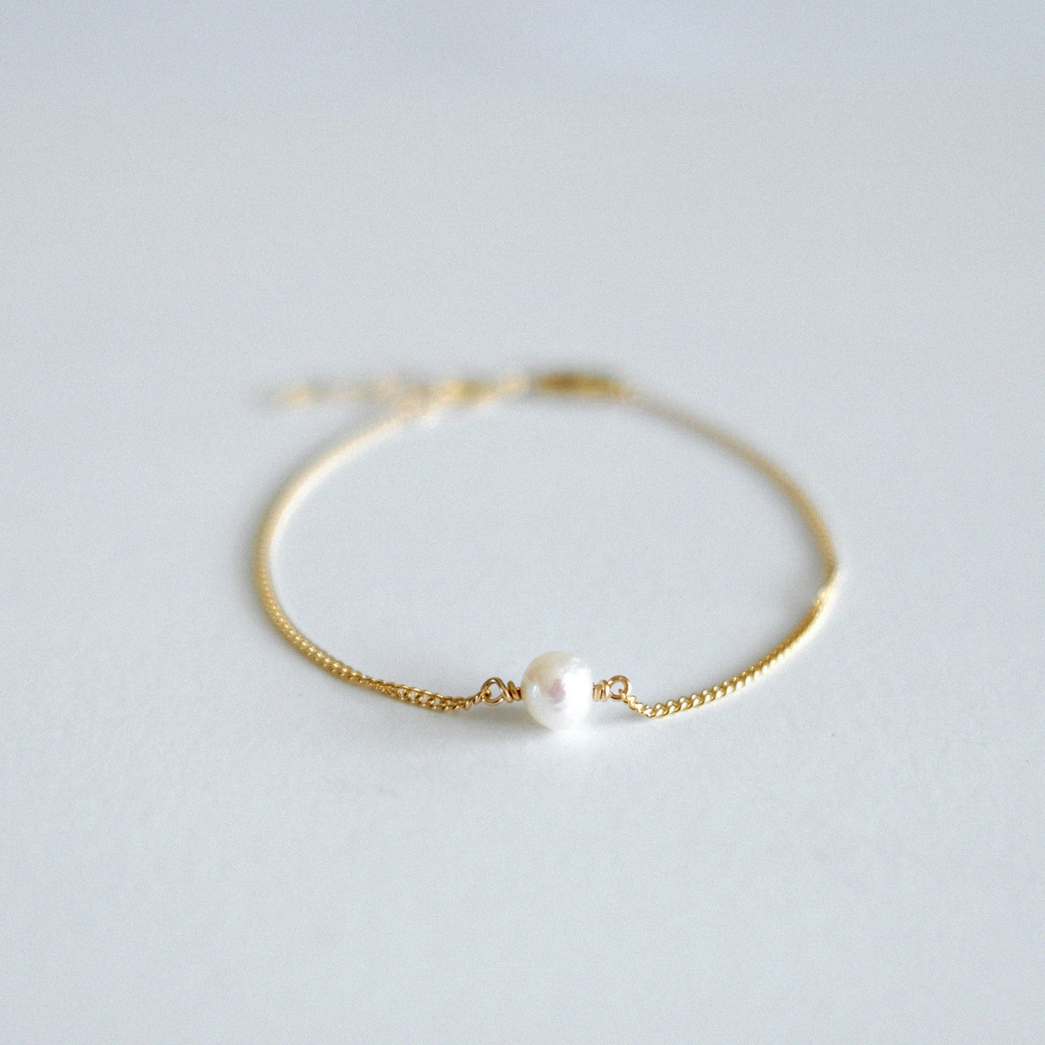 Gold bracelet with a pearl on a light gray background
