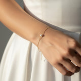 Gold bracelet with a pearl on a wrist against a neutral background