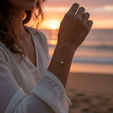 Person wearing a pearl bracelet on a beach at sunset