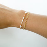 Gold bracelet with pearl-like beads on a wrist against a white background