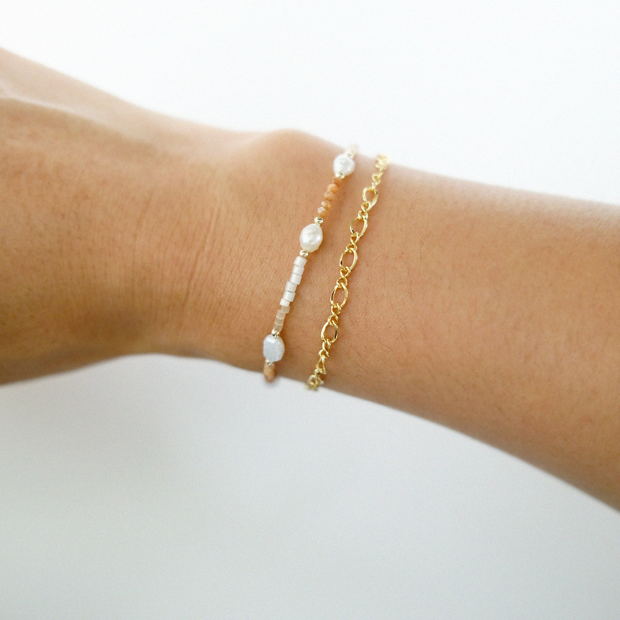 Gold bracelet with pearl-like beads on a wrist against a white background