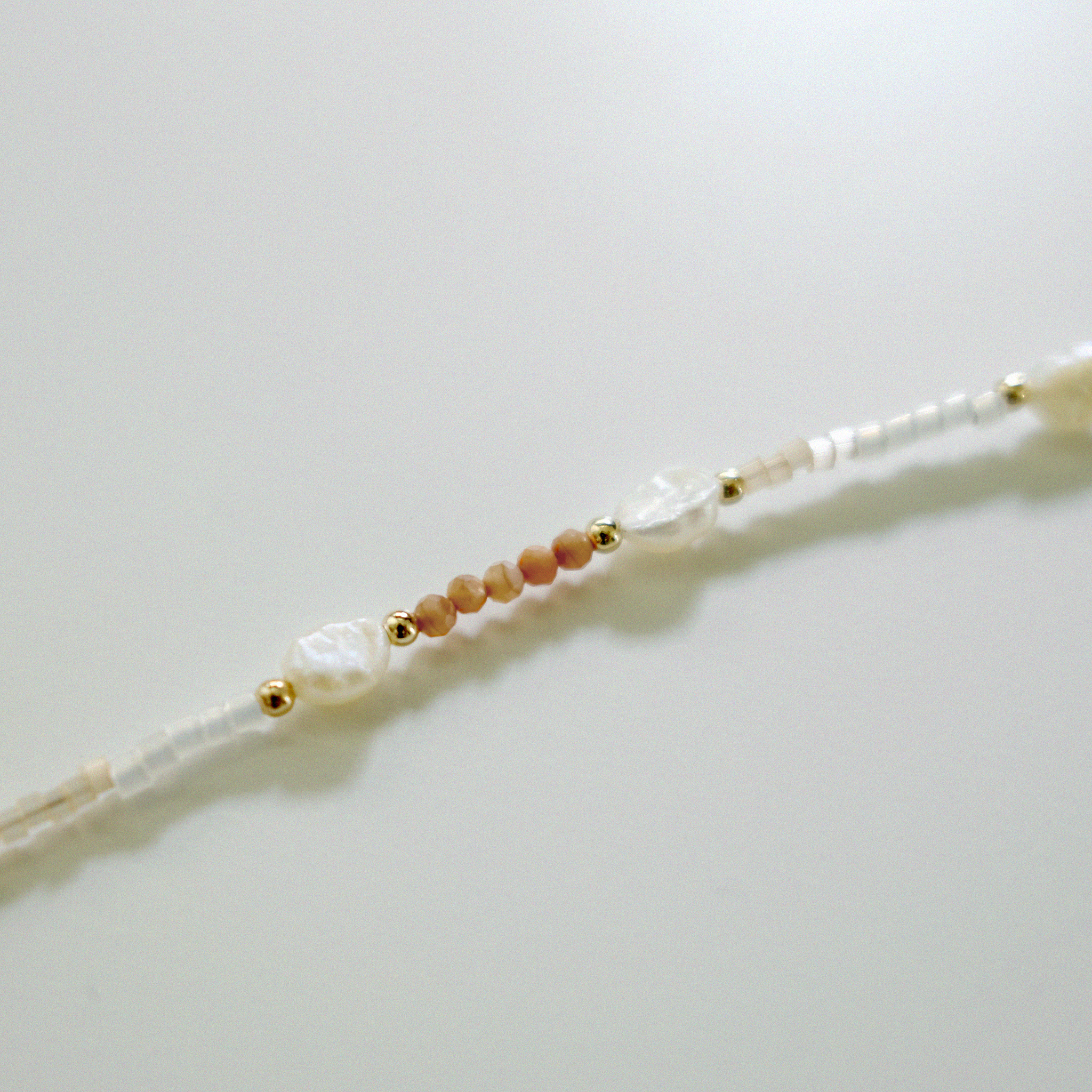 Beaded bracelet with pearls and gold accents on a light gray background
