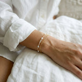 Close-up of a wrist wearing a gold bracelet with pearl-like beads, against a blurred background.