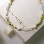 Beaded necklace with gold accents on a white cushion with 'LAONDRIM' branding.