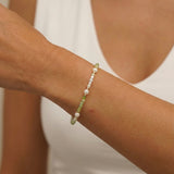 Close-up of a wrist wearing a bracelet with green and white beads against a neutral background