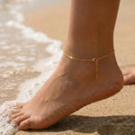 Gold anklet on a foot with sand and water in the background