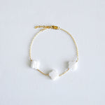 Gold bracelet with clover-shaped mother of pearl charm on a light gray background