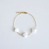 Gold bracelet with clover-shaped mother of pearl charm on a light gray background