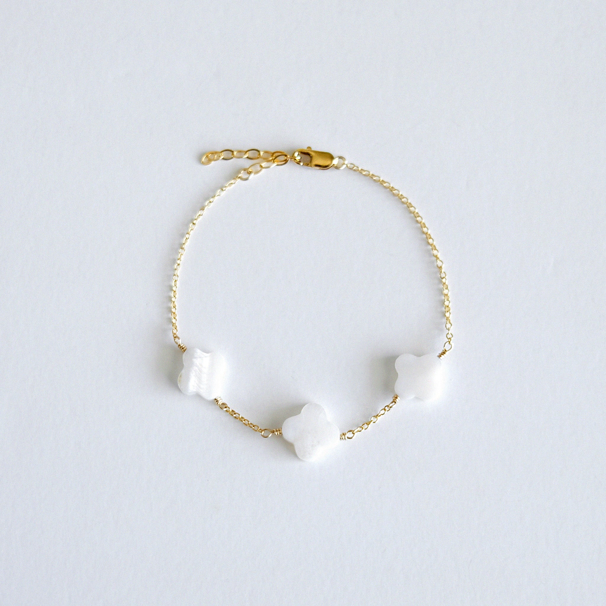 Gold bracelet with clover-shaped mother of pearl charm on a light gray background