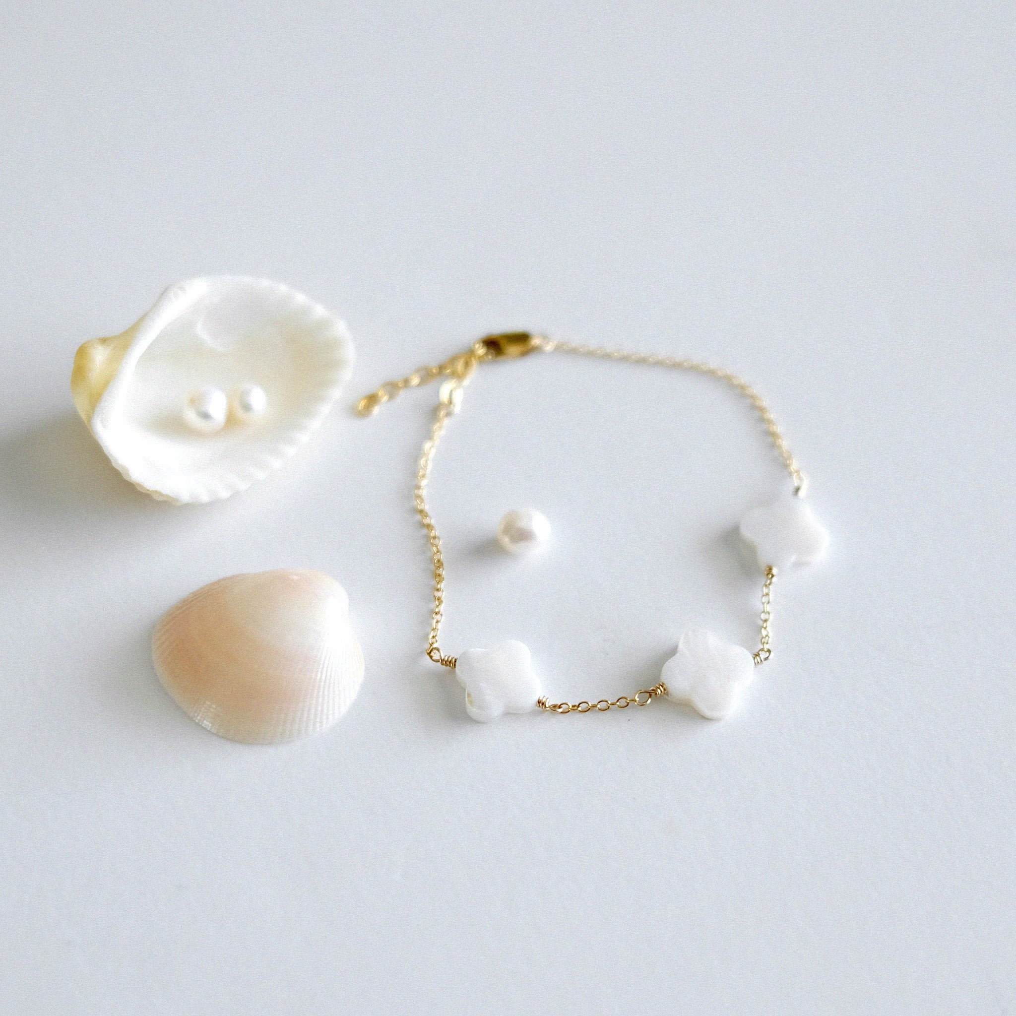 gold fille chain with clover-shaped charm bracelet with seashells and pearls on a light gray background