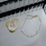 Gold bracelet with clover pendant on a white surface next to a shell