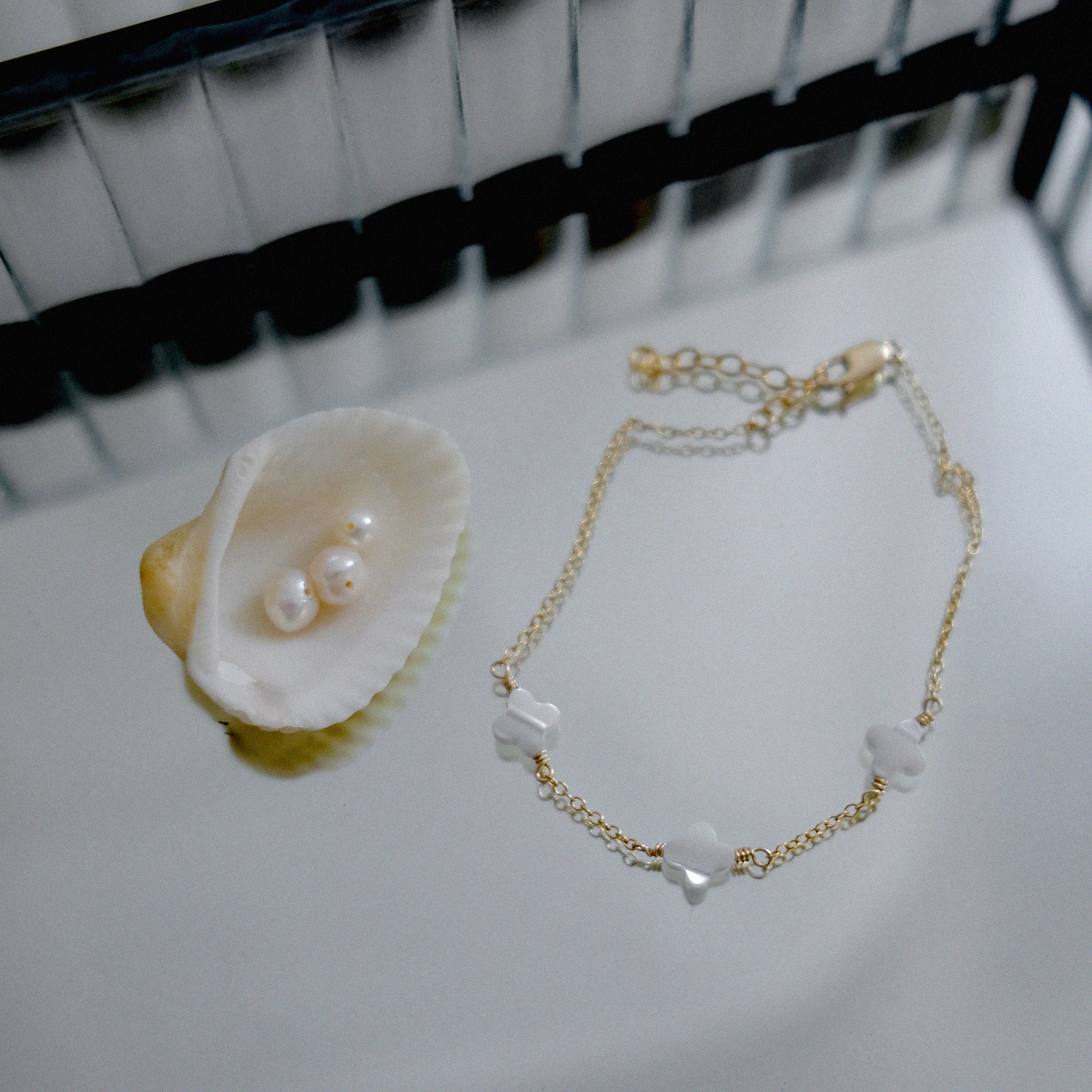 Gold bracelet with clover pendant on a white surface next to a shell