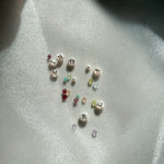 Small gemstones and mother of pearl initial charms on a reflective surface