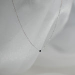 Delicate silver necklace with a small black pendant on a light gray background
